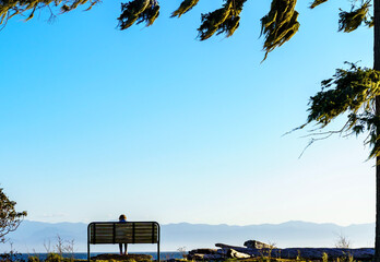 Lone person on bench on ocean shore with distant mountains 