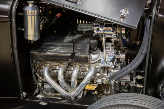 A slight downward view of a chromed engine in the body of a vintage auto 
