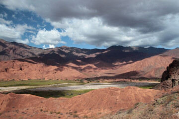 Desert landscape. Geology. View of the beautiful green valley surrounded by the red canyon sandstone mountains under a blue sky with clouds.
