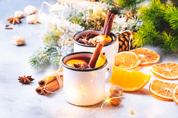 Mulled wine in white metal mugs with cinnamon, spices and orange with fir tree and christmas lights...