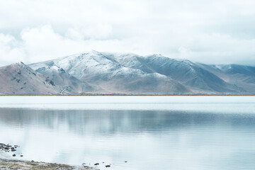 Snow mountain with reflection on lake and cloudy sky in blue tune.