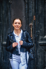 Fototapeta premium Portrait of a young beautiful woman in a leather jacket on the street of a European city