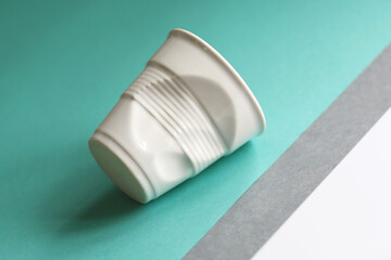 Reusable white ceramic glass looks like crumpled plastic glass on the colourful background. Sustainable lifestyle concept. Zero waste elements.