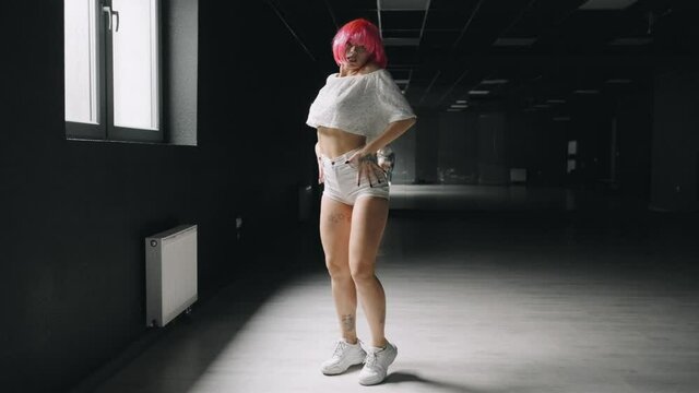 Hot girl is dancing at the dark studio background. Sexy pink woman is practicing dance