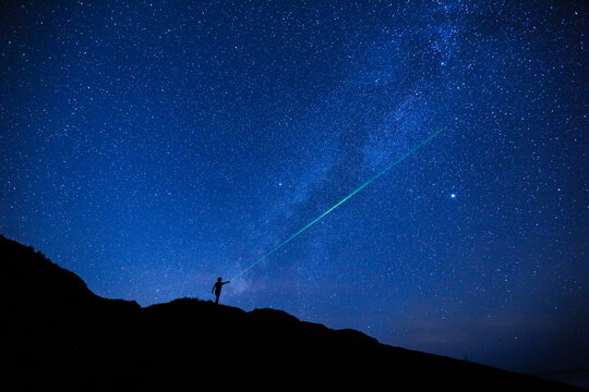 Silhouette of girl / woman standing on the hill use a laser pointer to point at a star.  Stargazing at Oahu island, Hawaii. Starry night sky, Milky Way galaxy astrophotography.