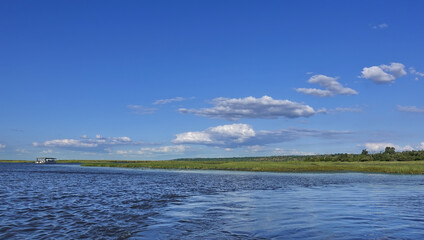Peaceful summer landscape. The blue river flows between green banks. There are clouds in the azure sky. The ship is visible in the distance. Botswana. Chobe.