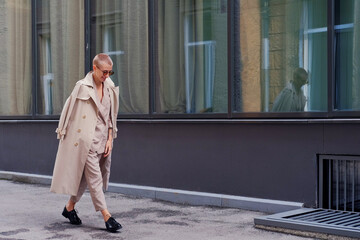 A woman with short hair in gray coat and glasses dancing, walking, smiling on a city street.