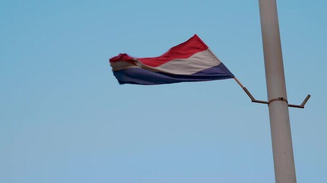 Flag with red, white and blue colors on a pole waving strongly in the wind