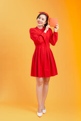 Happy young Asian woman showing gift box over orange background. Birthday, christmas, holiday, anniversary concept.