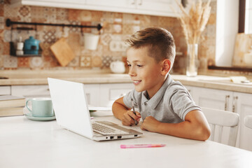 Naklejka na ściany i meble Boy does homework in the kitchen with a laptop online, talking to the teacher. Distance learning, online education,