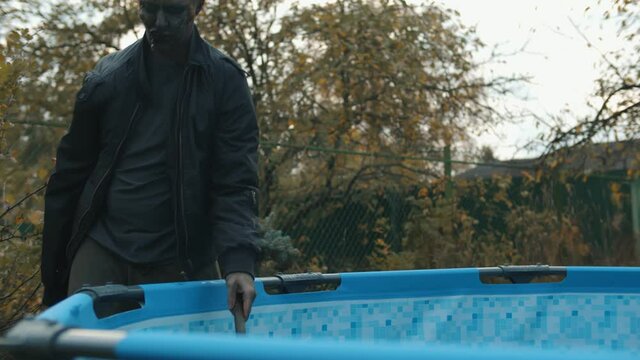 Zombie pool boy cleaning swimming pool with scoop-net in courtyard