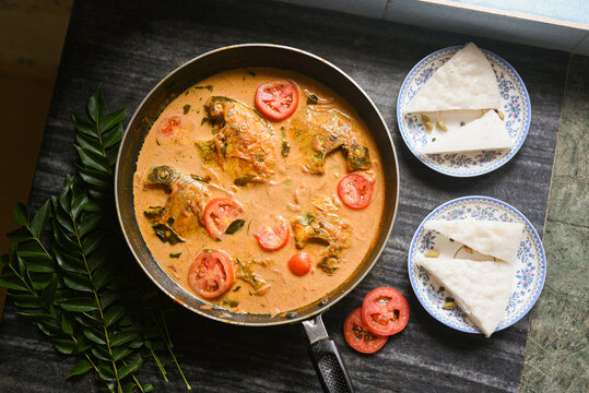 Top view spicy Kerala Style Fish stew and Appam Fish Molee or Meen Moilee Indian food. Fish curry with coconut milk red chili, curry leaf, tomato. Asian cuisine. Delicious hot Bengali, Goan fish curry