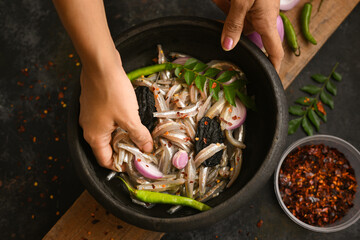 Top view spicy hot anchovy Kerala fish curry. Indian food. Woman hand making fish curry raw anchovies Malabar tamarind red chilli curry leaf. Asian cuisine. Delicious Bengali, Goan fish curry clay pot