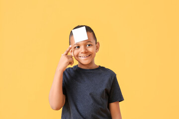 Little African-American boy with blank note paper on his forehead against color background