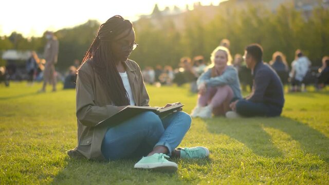 Happy african student lady reading book outdoors in park