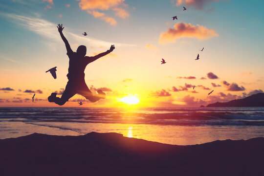 Happy man jumping at tropical beach with birds flying on sunset sky abstract background.