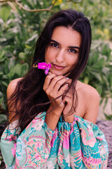 Fashion portrait of stylish woman in colorful print long sleeve top and pink shorts on beach, tropical background.  