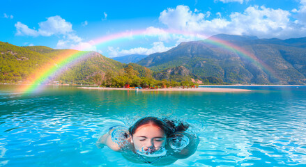 Obraz na płótnie Canvas Young girl swimming in Blue Lagoon of Oludeniz next to Mediterranean sea, Amazing rainbow in the background - Fethiye, Turkey