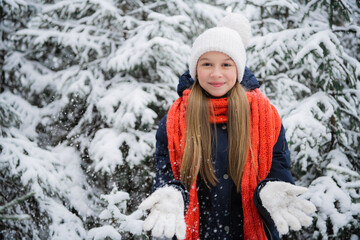 Fototapeta na wymiar A young teenage girl in a down jacket smiles beautifully for a picture in a winter snow covered forest.