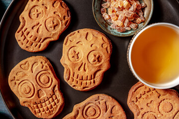 Halloween ginger cookies in the shape of skulls, close-up, homemade Dia de los muertos biscuits, overhead shot on a dark wooden background