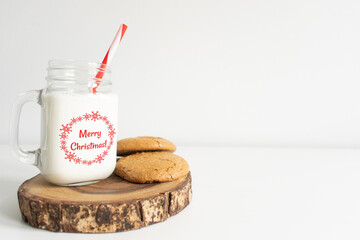 Merry Christmas old fashion milk jar. Mason jar with red striped straw and oatmeal cookies on white background. Christmas theme milk and cookies