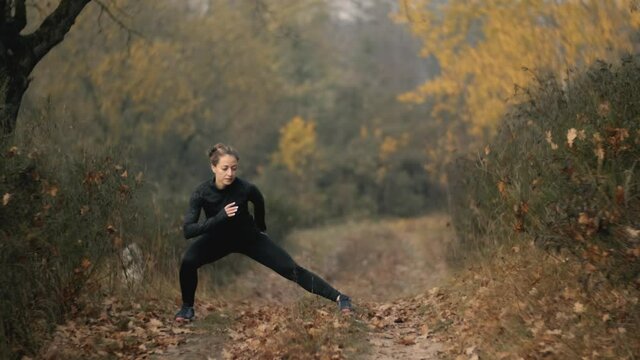 Runner woman is stretching legs with lunge hamstring stretch exercise leg stretches. Fitness female athlete is doing a warm-up before her strength training cardio workout.