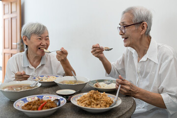 Happy smiling asian senior women eating Thai food,sitting at dining table in the house,old people...