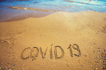 Inscription Covid 19 on the sand on the deserted beach. Pandemic concept