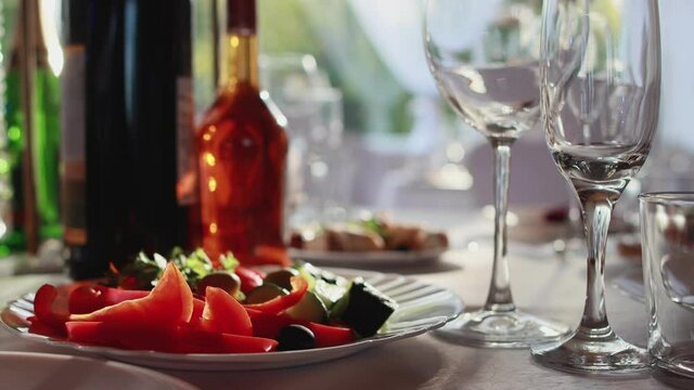 Beautiful table setting at a banquet, bottles with alcohol glasses stand on a decorated table against the background of the sun