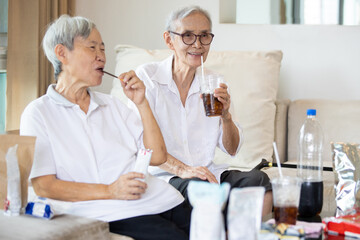 Two elderly people drinking soft drink,eat junk food,bottle of soda drink and snacks on the table...