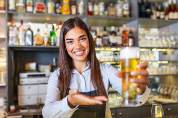 Beautiful smiling female Bartender serving a draft beer at the bar counter , shelves full of bottles with alcohol on the background