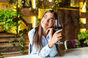 Image of cute pretty young woman sitting in cafe holding glass and drinking wine. portrait of a beautiful wine tasting tourist woman.