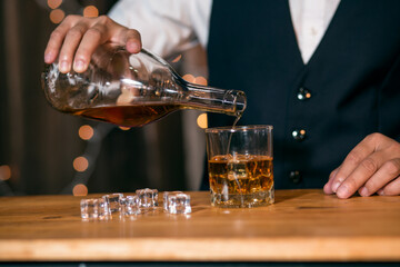 Waitress man standing pours whiskey into a glass 