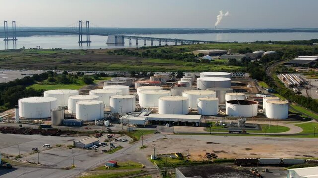 Aerial of oil and gas fuel refinery storage tanks at Wilmington USA port, Delaware Memorial Bridge in distance. Tractor trailer truck arrives to pick up load of gasoline or diesel for distribution.