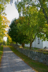 Road with a stone wall at the church on the island Adelsö at autumn in Stockholm

