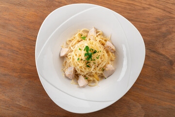 Alfredo spaghetti pasta with chicken fillet and sauce on a white plate on a wooden background, top view