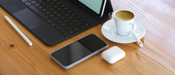 Workspace with smartphone, tablet, stylus and coffee cup on wooden table