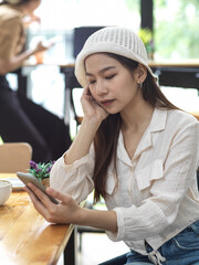 Female college student relaxing with smartphone while doing homework in cafe