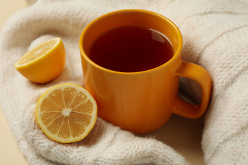Sweater with cup of tea and lemons on beige background