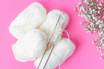 White yarn and knitting needles on pink background top view.