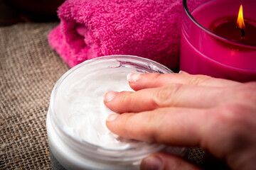 Female hand takes cream. Spa composition of pink aromatic candle and towel on wooden background.