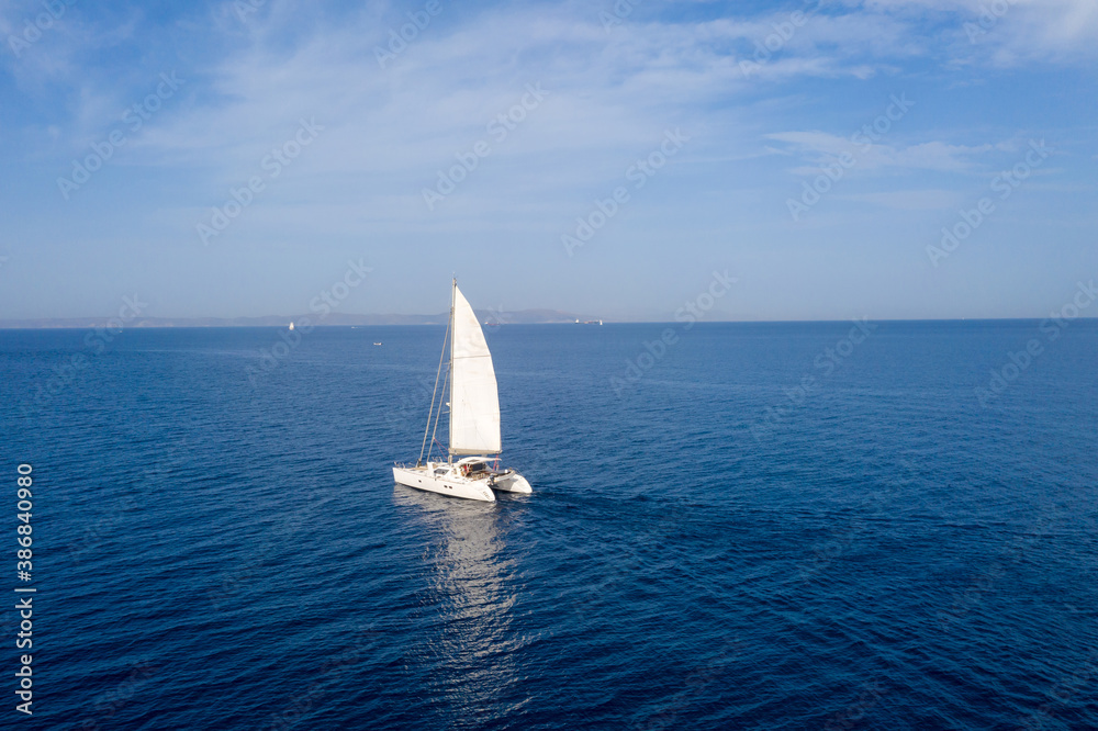 Wall mural sailing boat catamaran with white sails, cloudy sky and rippled sea background