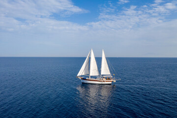Fototapeta premium Sailing boat with white sails in the open sea, cloudy blue sky