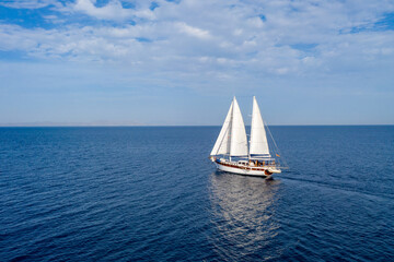 Sailing boat with white sails in the open sea, cloudy blue sky