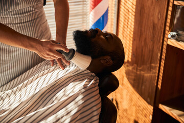 Barber brushing off hair around client neckline after beard trimming