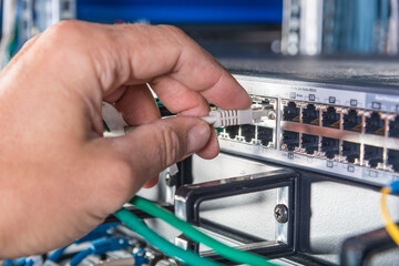 hand of engineer plugging in ethernet cable into server switch