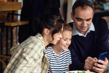 A father is showing somthing to his family on his phone while they ar esitting at the table.