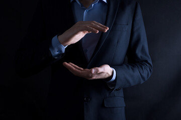 An empty workpiece. A businessman in a suit on a black background holds his hands protective gesture. A gesture of care and patronage.
