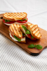 Tasty Grilled Caprese Panini (Mozzarella, Tomatoes and Basil) on a rustic wooden board, side view.