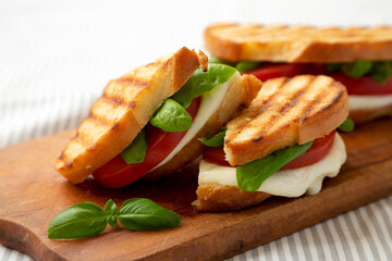 Tasty Grilled Caprese Panini (Mozzarella, Tomatoes and Basil) on a rustic wooden board, side view. Close-up.